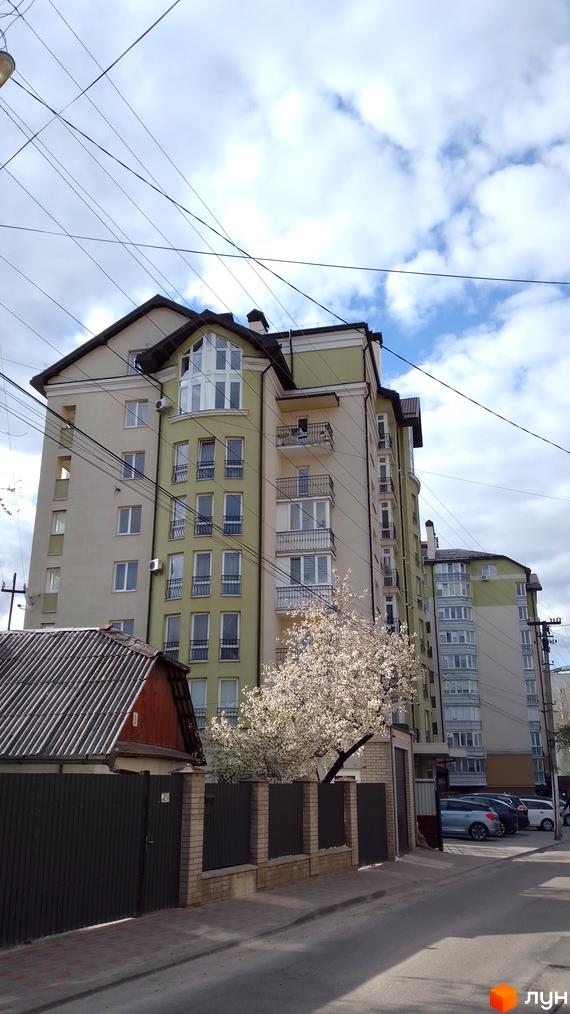 Зовнішній вигляд багатоповерхового будинку на вулиці Вояків Дивізії Галичина. На передньому плані огорожа та квітуче дерево.