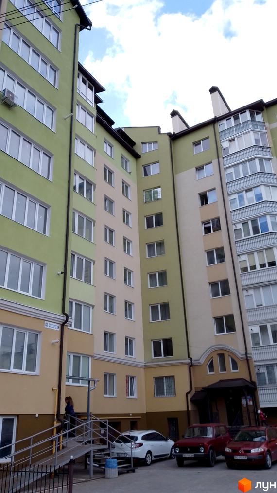 Зображення фасаду багатоповерхового будинку на вулиці Вояків Дивізії Галичина. На передньому плані припарковані автомобілі.