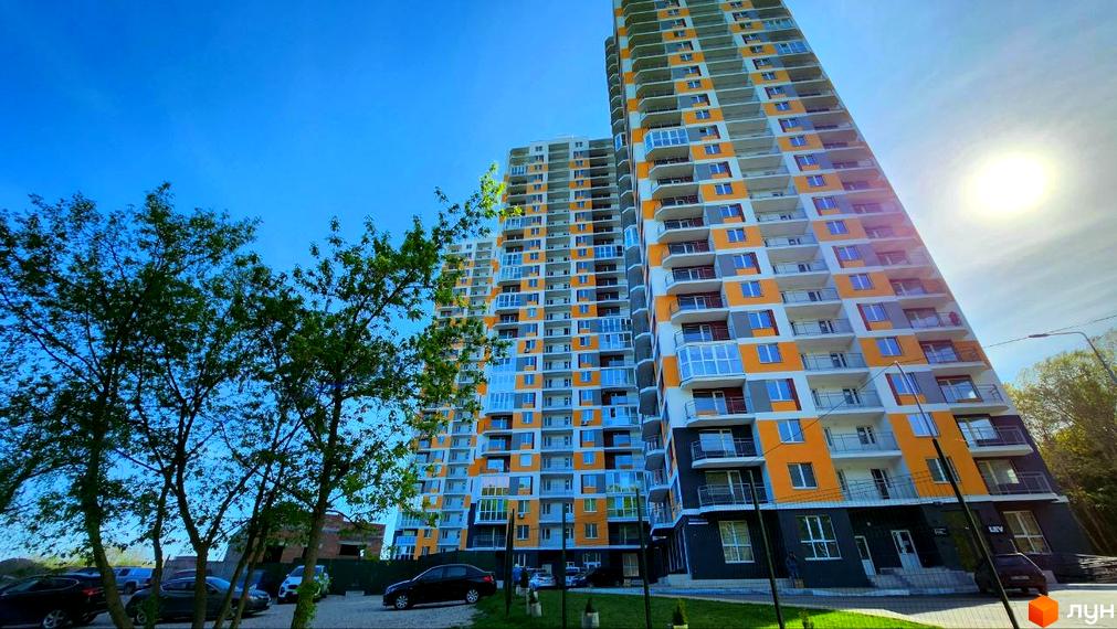 Житловий комплекс Orange City з яскравим фасадом та балконами. Територія біля будинку з деревами та припаркованими автомобілями.
