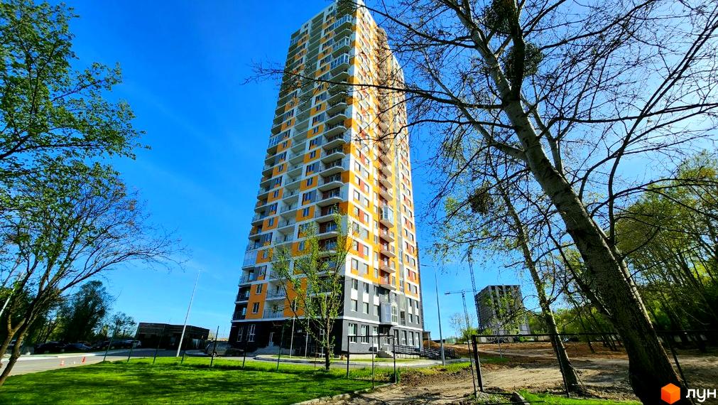 Високоповерховий житловий комплекс Orange City з яскравим фасадом та балконами. Навколо зелена територія з деревами та будівельним майданчиком.