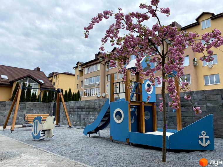 Клубний будинок Васильченка: дитячий майданчик у вигляді корабля та гойдалки на тлі багатоповерхових будинків.