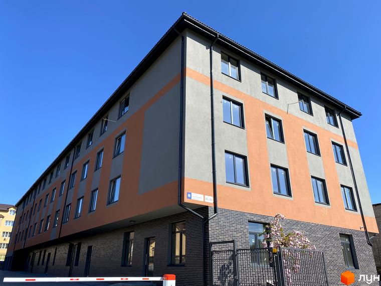 Клубний будинок „Васильченка“ з сірим та помаранчевим фасадом, вікнами та цегляним цоколем. На передньому плані паркан та шлагбаум.