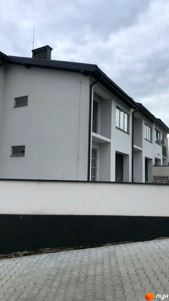 Білі будинки з темною покрівлею та вікнами. Перед будинками розташована біла огорожа та бруківка.