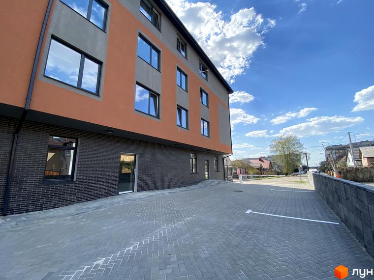 Клубний будинок „Васильченка“ з цегляним цоколем та помаранчевими фасадами, облаштований паркінг з розміткою.