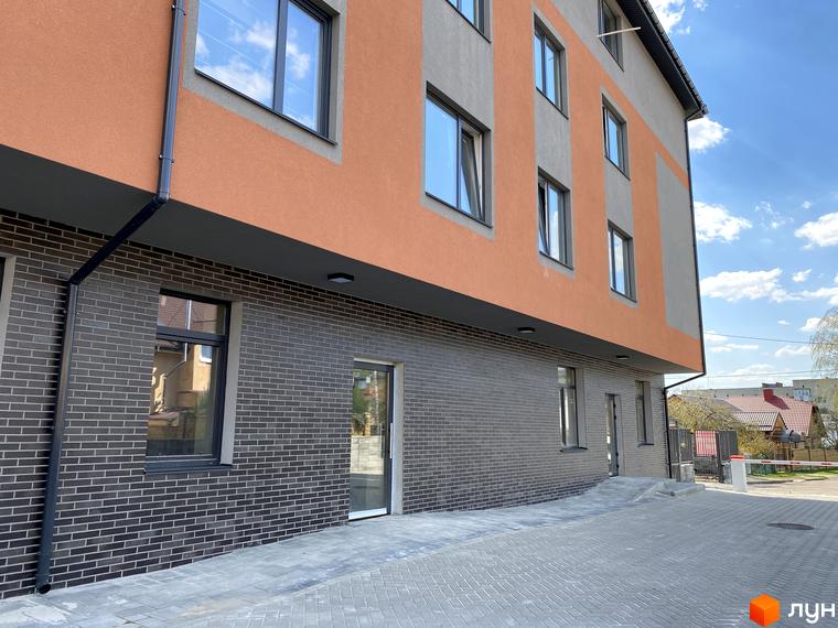 Клубний будинок Васильченка з фасадом з помаранчевої та сірої штукатурки, сірої цегляної кладки та вхідною групою. Прибудинкова територія з бруківки та парканом.