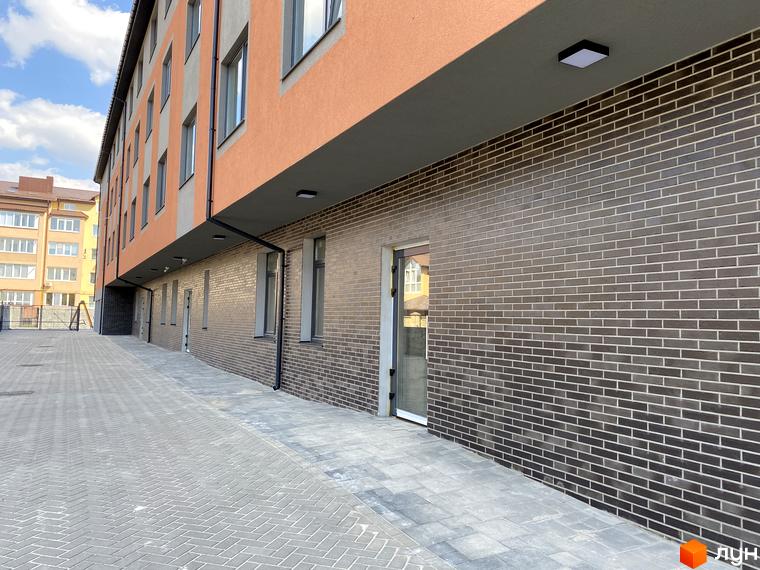 Клубний будинок Васильченка з цегляним фасадом та вимощеною прибудинковою територією. Зовнішній вигляд новобудови з вікнами та дверима.