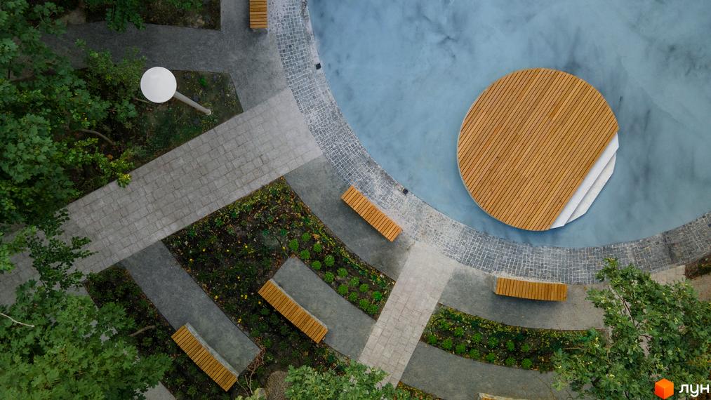 Житловий комплекс Chalet: оглядовий вид на зону відпочинку з дерев'яним круглим настилом, лавками та водоймою.