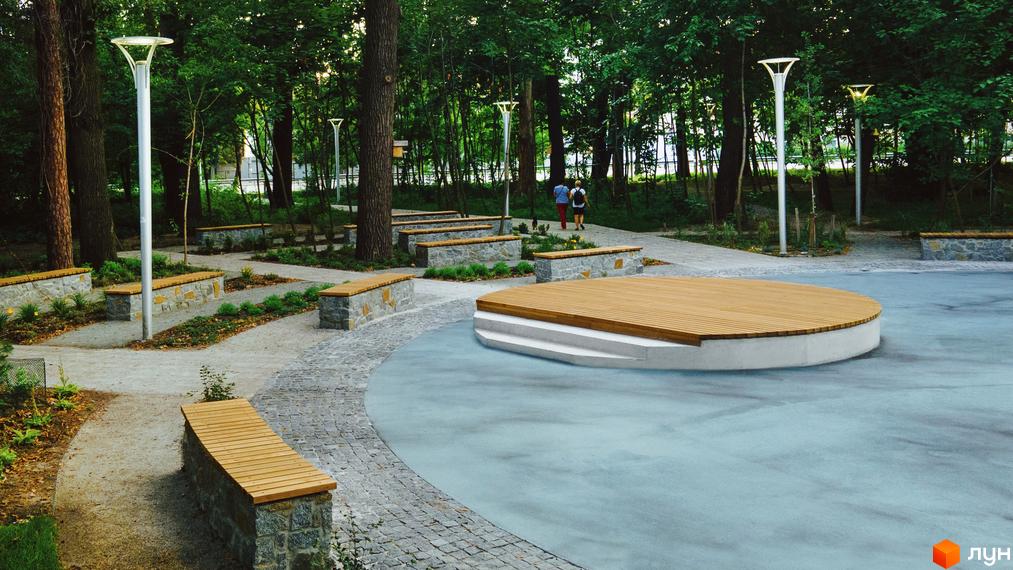 Зона відпочинку в житловому комплексі Chalet з дерев'яною сценою та лавками. Паркова зона з освітленням та пішохідними доріжками.