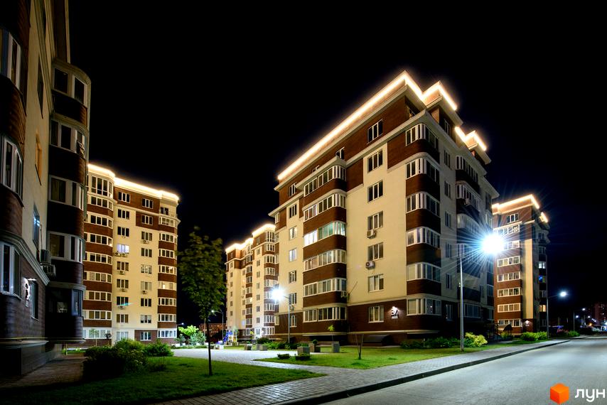 Нічний вид на будівлі ЖК Золота Ера. На фото видно освітлені будинки з вікнами та прибудинкову територію з газонами та деревами.