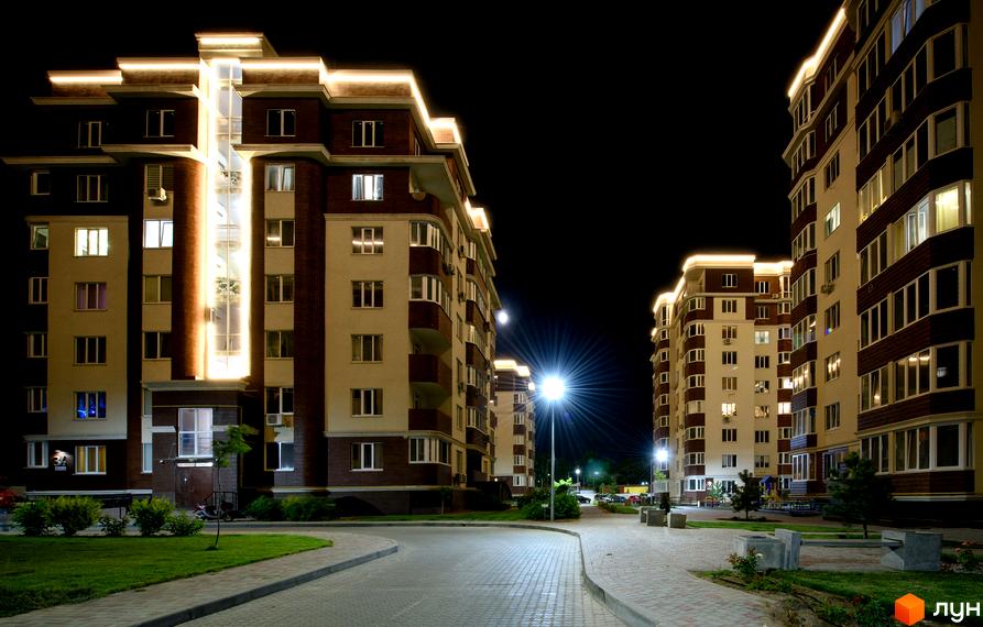 Житловий комплекс Золота Ера вночі з підсвічуванням. Високі будинки з вікнами, освітлені ліхтарями, та бруківка на прибудинковій території.