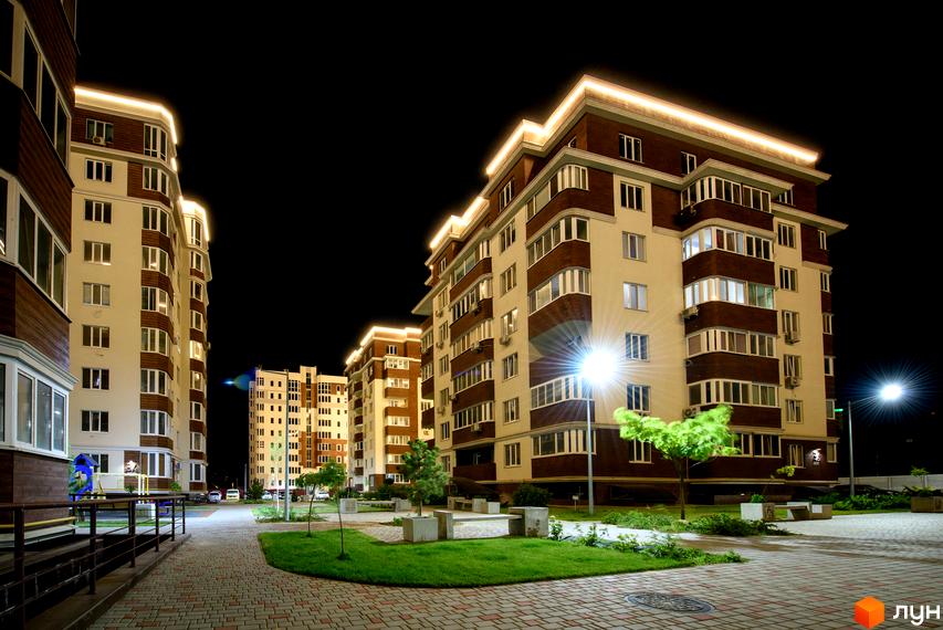 Житловий комплекс Золота Ера з підсвічуванням у вечірній час. Доглянута прибудинкова територія з газонами та тротуарами.