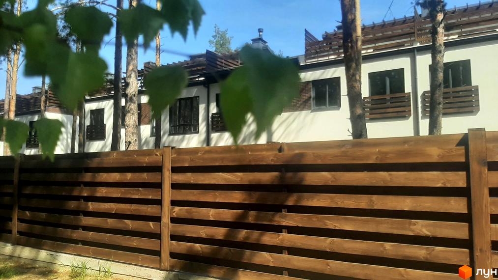 Котеджне містечко КМ Лісове-3. Зовнішній вигляд будинків з дерев'яними елементами та парканом з дерева. Прибудинкова територія з деревами.