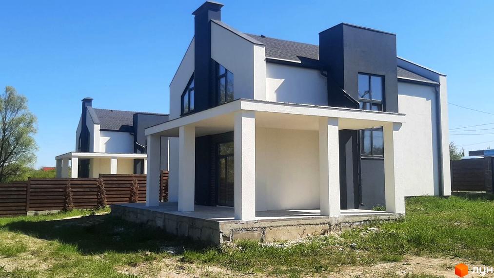 Білий будинок з чорними елементами та великими вікнами. На передньому плані газон та дерев'яний паркан.