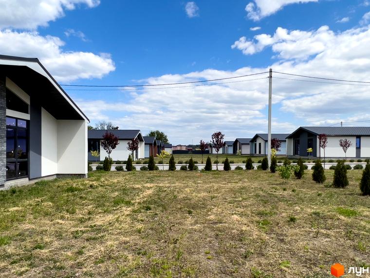 Зображення котеджів у Містечку котеджів Millennium House. На фото видно будинки з білими стінами та темними дахами, розташовані на доглянутій території з газоном.