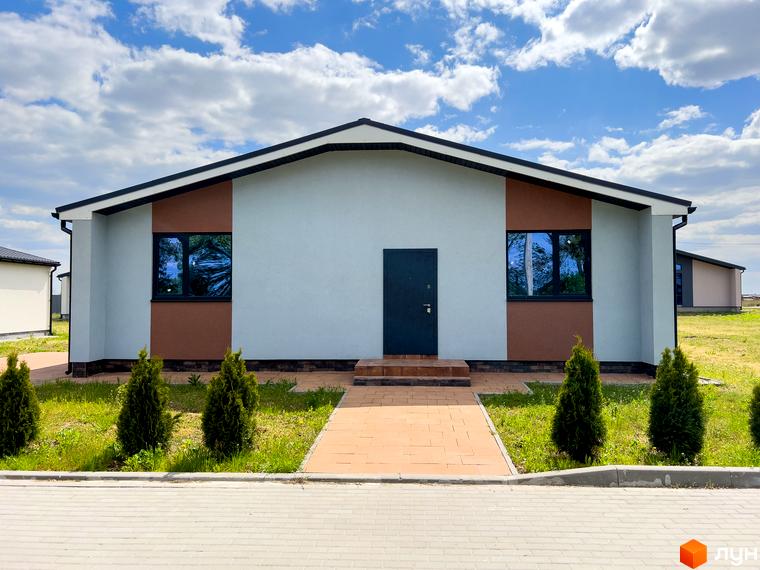 Фасад будинку Котеджного містечка Millennium House у світло-сірих та коричневих тонах з темними вікнами. Перед будинком зелений газон з туями та вимощена доріжка.