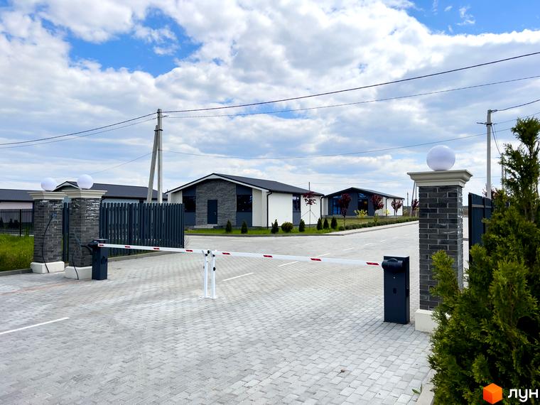 В'їзд до Котеджного містечка Millennium House зі шлагбаумом. Видно одноповерхові будинки з темними дахами та комбінованими фасадами.