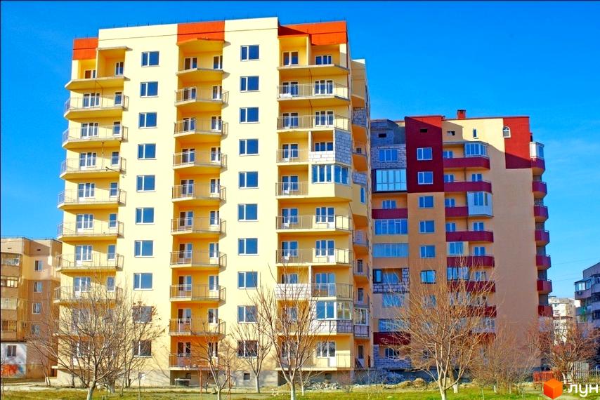 Житловий комплекс Таврійський з жовтою фасадною частиною та великими балконами. Прибудинкова територія з деревами та газоном.
