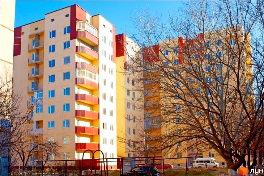 Житловий комплекс Таврійський з яскравими фасадами та балконами. Прибудинкова територія з дитячим майданчиком та деревами.