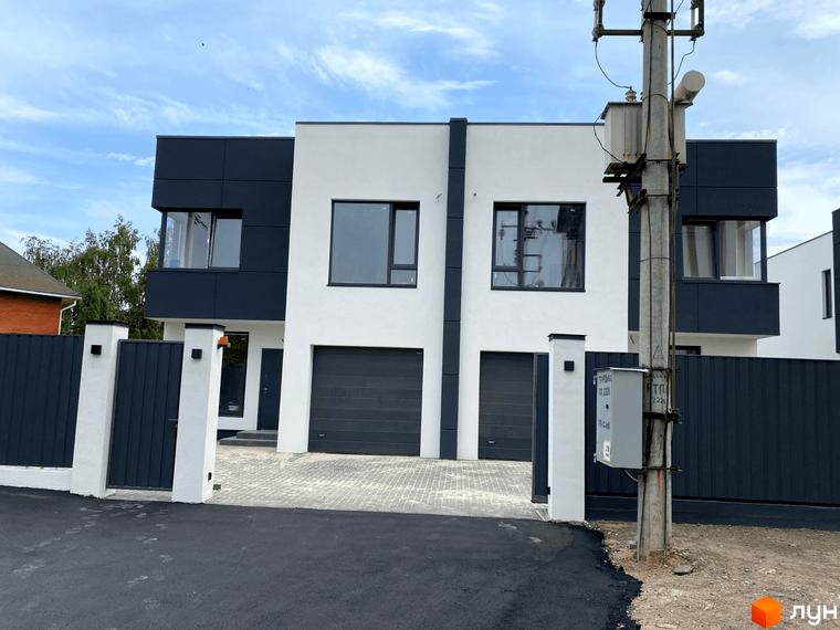 Зовнішній вигляд будинку ЖК по вул. Пшенична, 20 з темними фасадами та гаражами, огороджений парканом з білими колонами, асфальтована дорога.