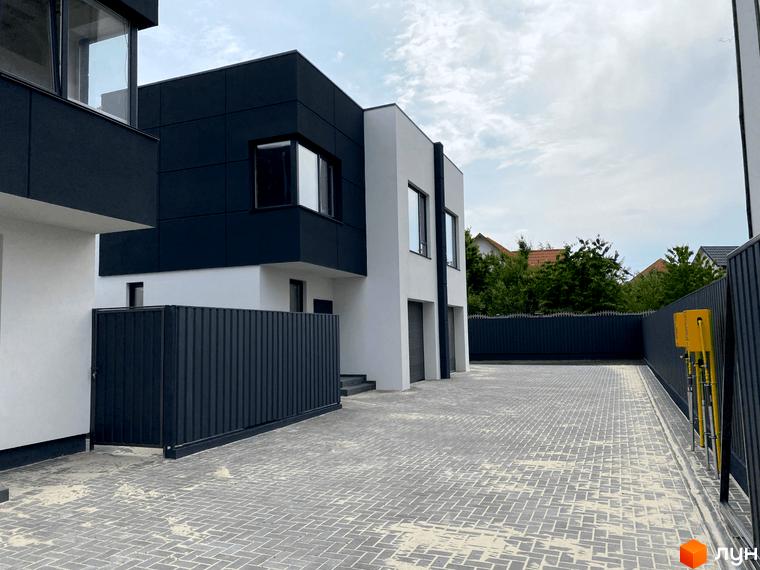 Зовнішній вигляд будинку з темним фасадом та білими стінами. На передньому плані - бруківка та огорожа. ЖК на вулиці Пшенична, 20.