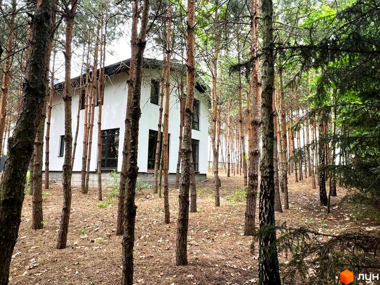 Вигляд двоповерхового будинку з великими вікнами в Котеджному містечку GREEN CLUB, оточеного сосновим лісом.