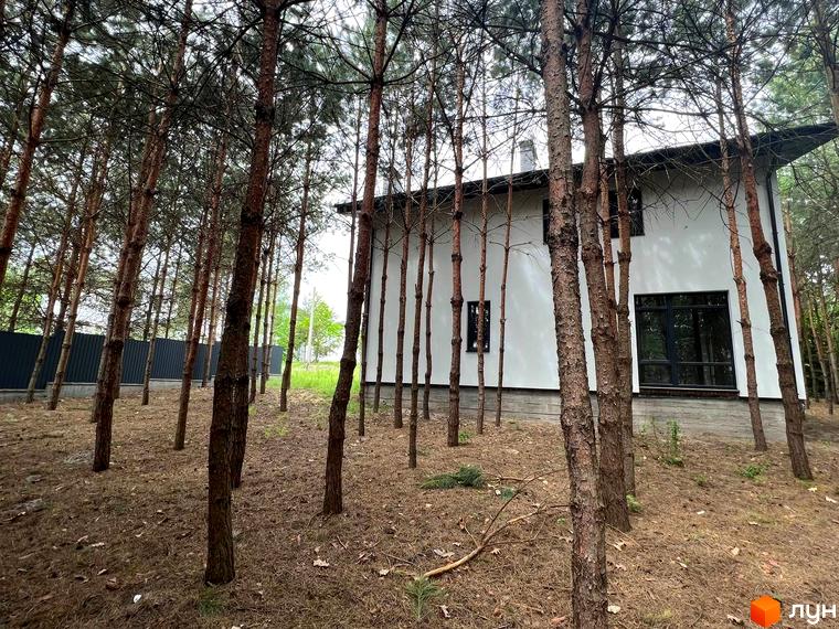 Зображення будинку в Котеджному містечку GREEN CLUB серед соснового лісу. Навколо будинку дерева та опале листя.