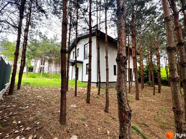 Зображення будинку в Котеджному містечку GREEN CLUB, оточеного сосновим лісом. Навколо будинку видно опале листя та хвою.