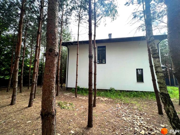 Вигляд будинку в Котеджному містечку GREEN CLUB з великими вікнами та темним дахом. Навколо будинку ростуть сосни.