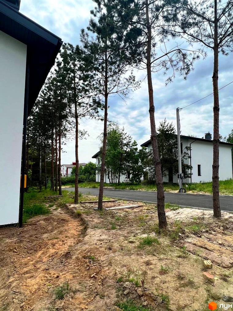 Зовнішній вигляд будинку в Котеджному містечку GREEN CLUB. Навколо будинку дерева та піщаний ґрунт.