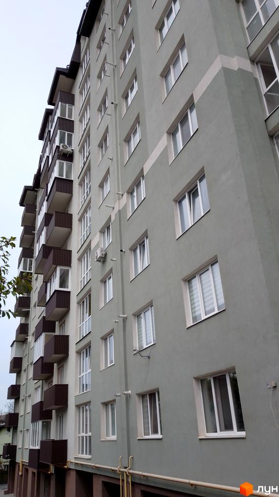 Висотна новобудова з балконами та панорамними вікнами. Фасад будинку пофарбований у сірий колір з білими вставками.