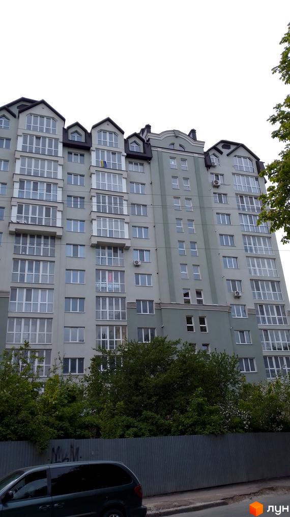 Багатоповерховий житловий будинок на вул. Глибока, 24 з балконами та українським прапором. Перед ним зелені дерева та металевий паркан.