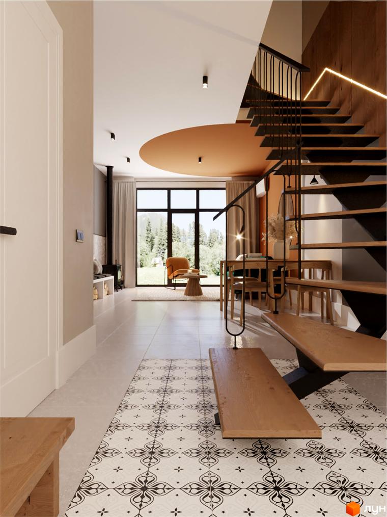 Інтер'єр вітальні з каміном та великими вікнами, що виходять на ліс. Сучасні сходи з дерев'яними сходинками та металевим поручнем ведуть на другий поверх.