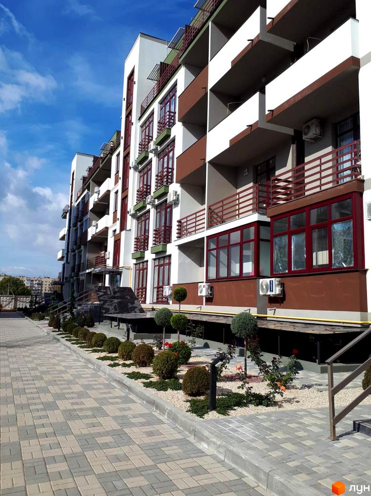 Будівельний проєкт Smart City з біло-коричневим фасадом та балконами. Поруч розташована вимощена доріжка та зелені насадження.