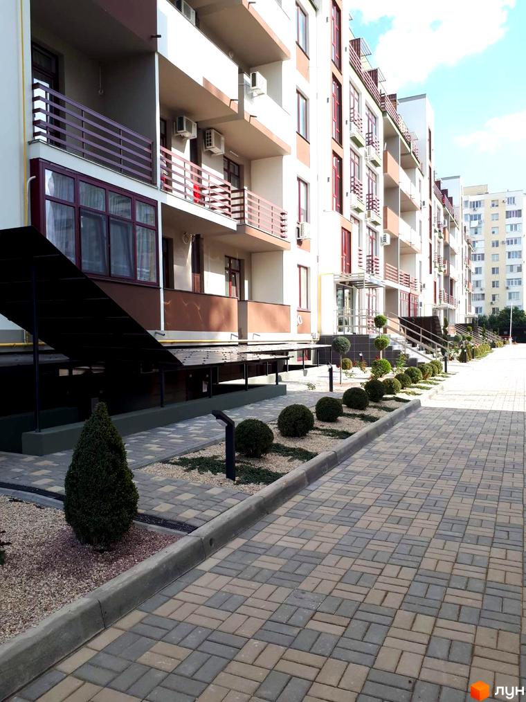 Житловий комплекс Smart City з фасадами світлих кольорів та балконами з червоними поручнями. Прибудинкова територія з бруківкою та зеленими насадженнями.