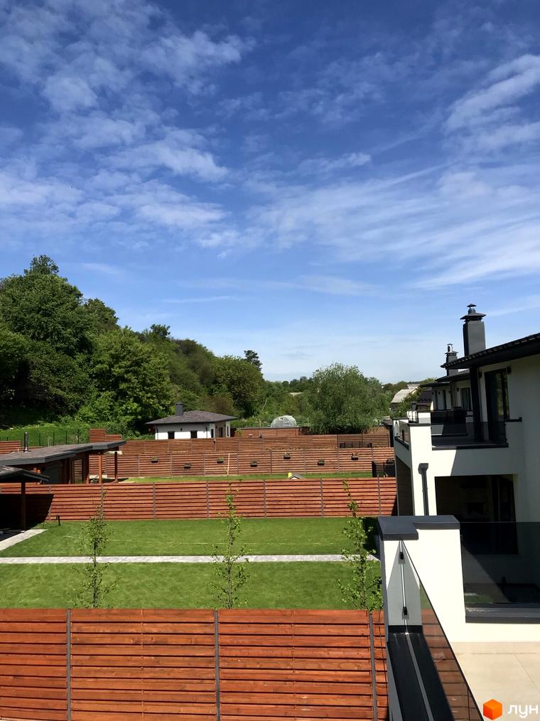 Котеджне містечко Lugovoy. Зовнішній вигляд будинків та доглянута прибудинкова територія з газоном та дерев'яними парканами.