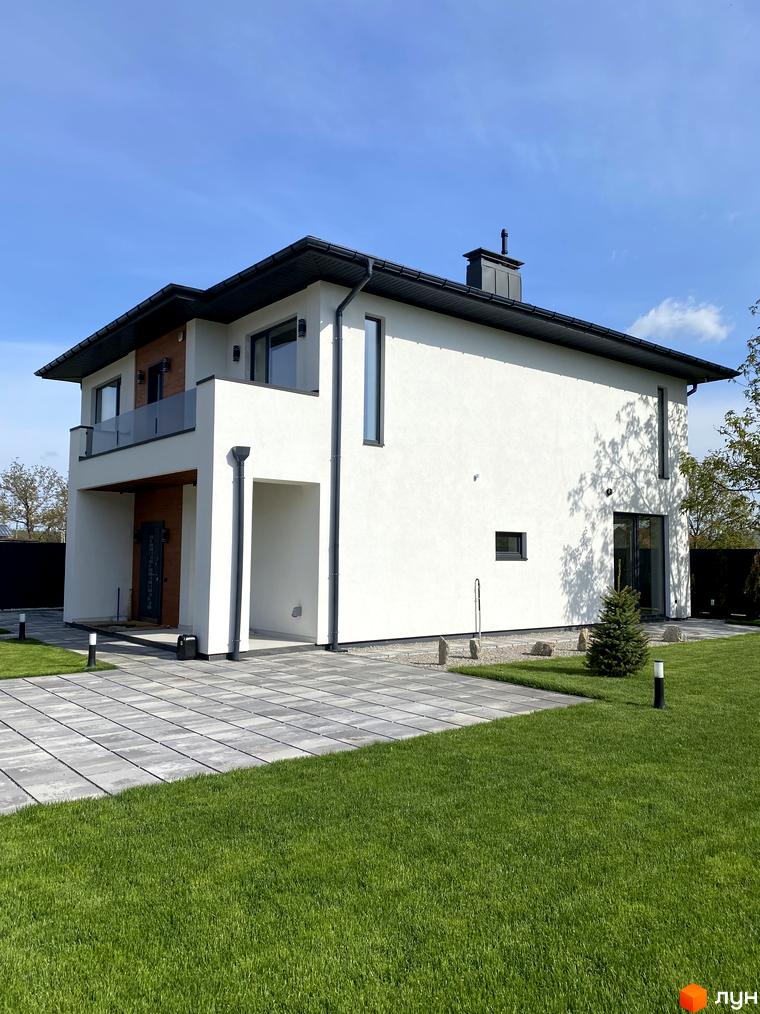 Сучасний двоповерховий будинок з білою фасадною штукатуркою, чорною даховою системою та великими вікнами. Прибудинкова територія з акуратним газоном та вимощеною плиткою доріжкою.