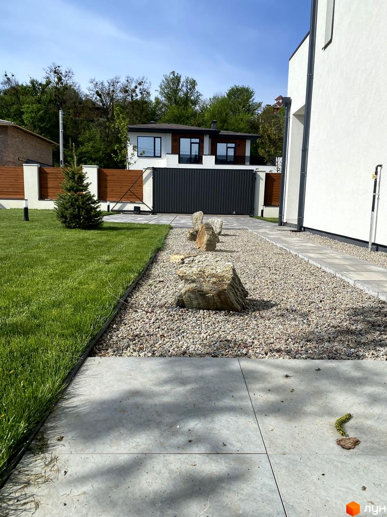 Зовнішній вигляд будинку та прибудинкової території комплексу Lugovoy. Зелений газон, доріжка з плитки та декоративні камені.