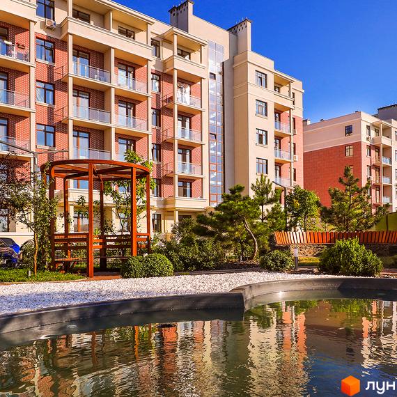 Житловий комплекс Парк Совіньйон. Зовнішній вигляд будівель з червоної цегли та світлої штукатурки, балконами та скляними елементами. Прибудинкова територія з водоймою, зеленню та дерев'яною альтанкою.
