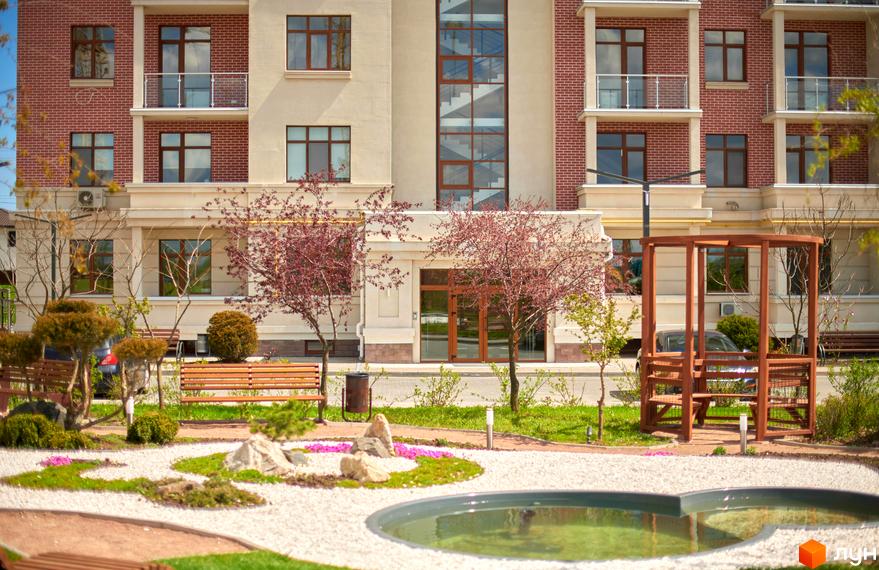 Житловий комплекс Парк Совіньйон. Фасад будинку з цегляними та світлими елементами, вікнами та балконами. Прибудинкова територія з ландшафтним дизайном, зонами відпочинку та водоймою.