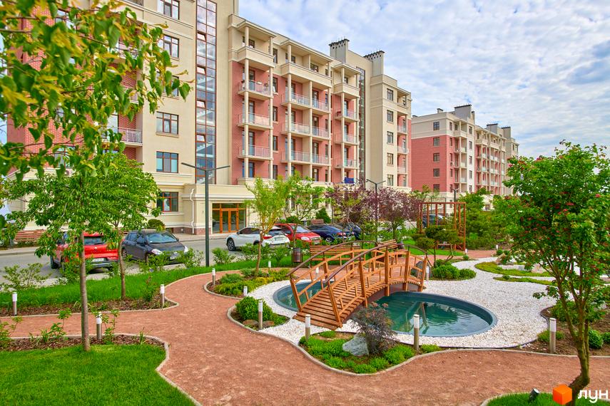 Житловий комплекс Парк Совіньйон з фасадами оздобленими цеглою та балконами. Доглянута прибудинкова територія з доріжками, деревами та декоративним водоймищем з містком.