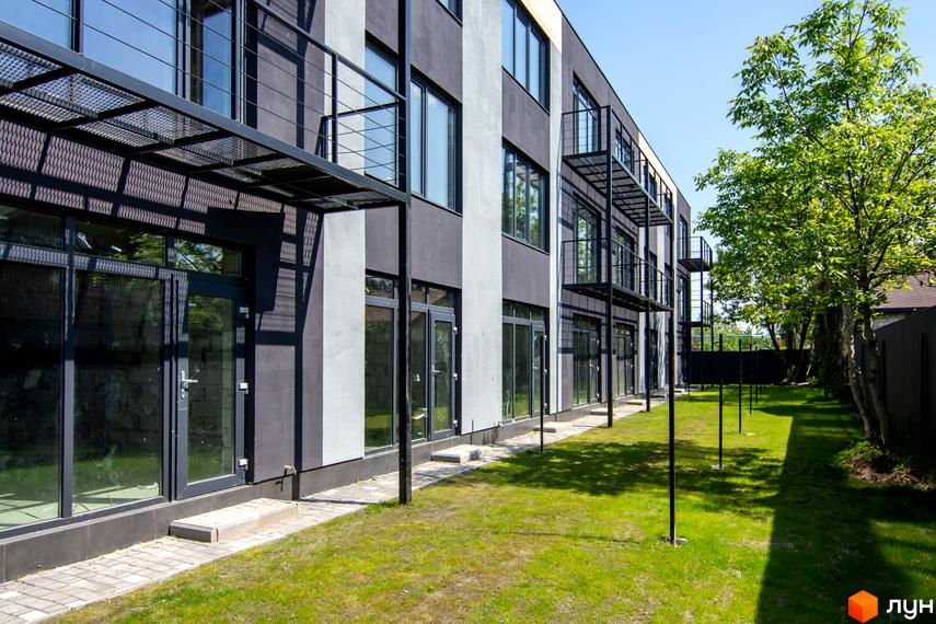 Фасад таунхаусів Rusaniv Gardens з чорними балконами і великими вікнами. Доглянута прибудинкова територія з газоном та деревами.