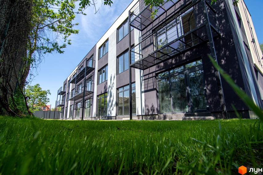 Фасад таунхаусів Rusaniv Gardens з великими вікнами та металевими балконами. Перед будинком розкинувся зелений газон.