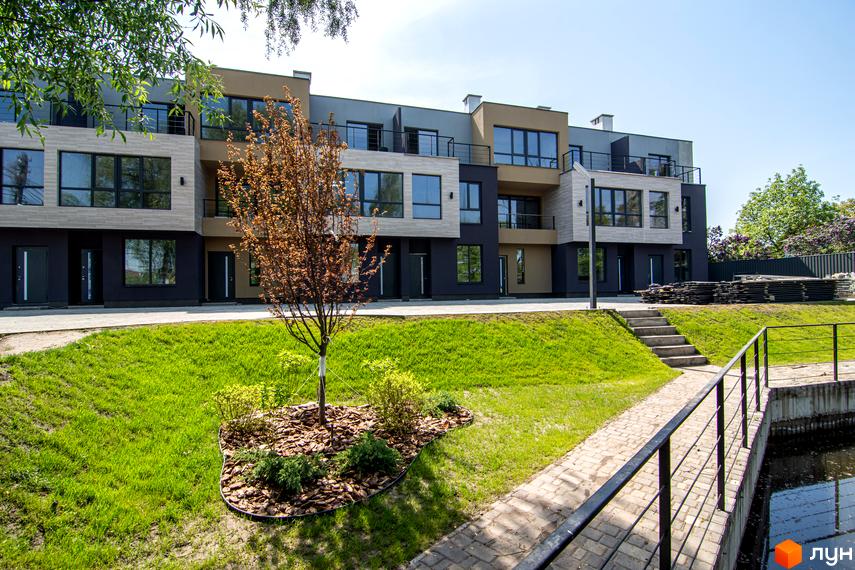 Зовнішній вигляд таунхаусів Rusaniv Gardens з великими вікнами та балконами. На території комплексу газон, доріжки та декоративні дерева.
