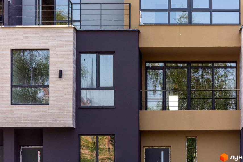 Фасад будинку житлового комплексу Rusaniv Gardens з великими вікнами та балконами. Видно оздоблення стін різними матеріалами.