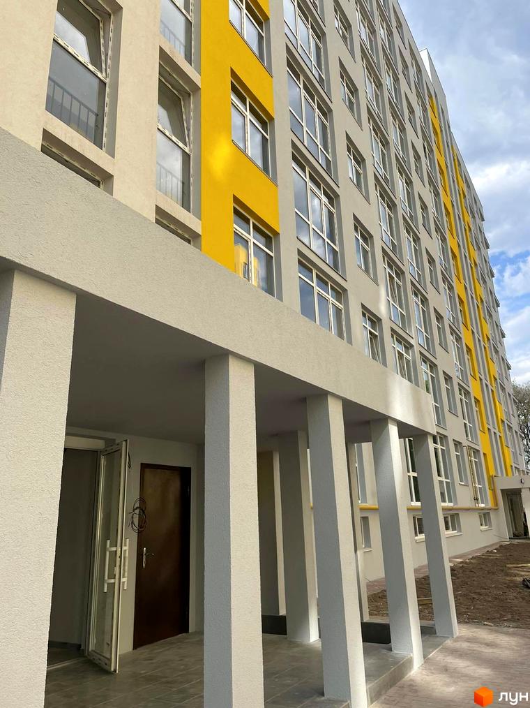 Житловий комплекс Обухівський ключ. Багатоповерховий будинок з фасадом світлого кольору з жовтими акцентами. На першому поверсі розташований вхід з колонами.