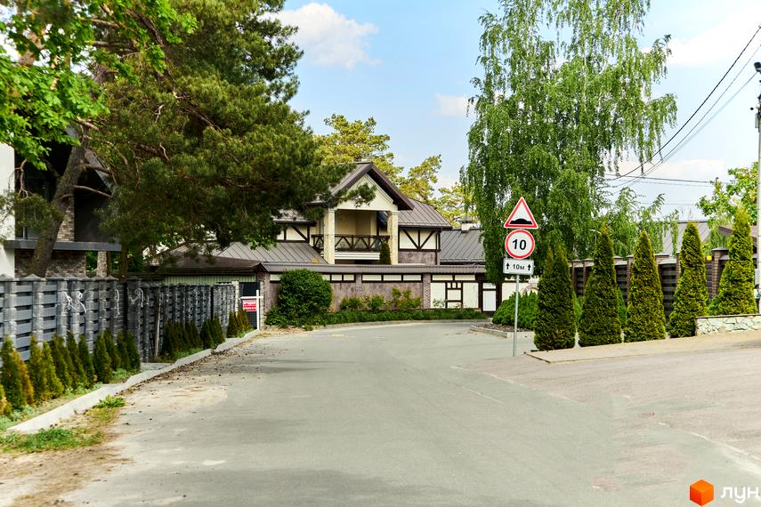 Котеджний комплекс Квітка Полонини з двоповерховим будинком з балконом та огородженою територією. На території ростуть дерева та кущі, є дорога.