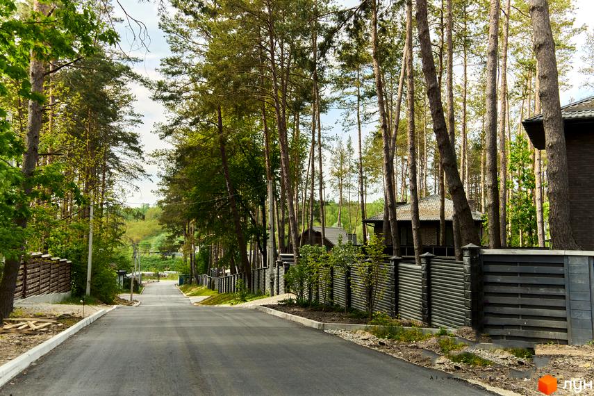 Вулиця в котеджному містечку Квітка Полонини з будинками за парканом та високими деревами.