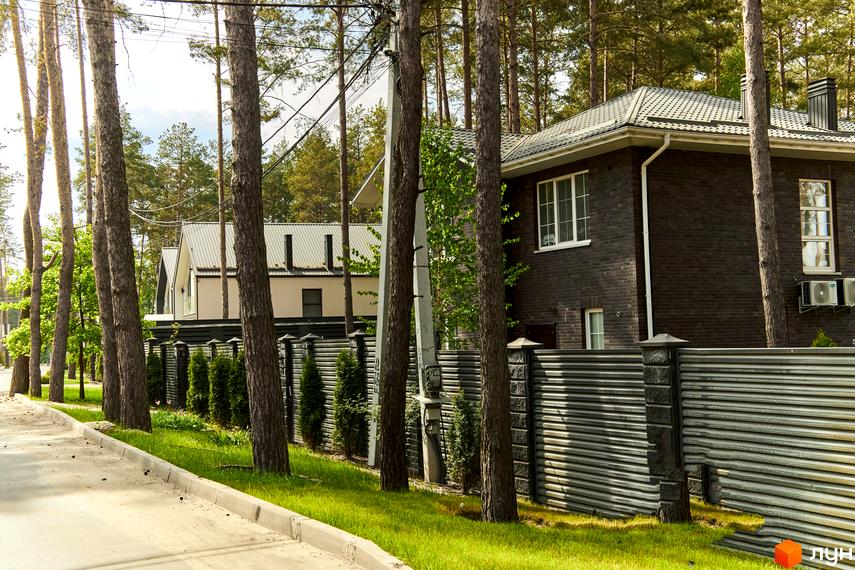 Цегляний будинок з білими вікнами та металевим парканом в Котеджному містечку Квітка Полонини. Доглянута прибудинкова територія з деревами та газоном.