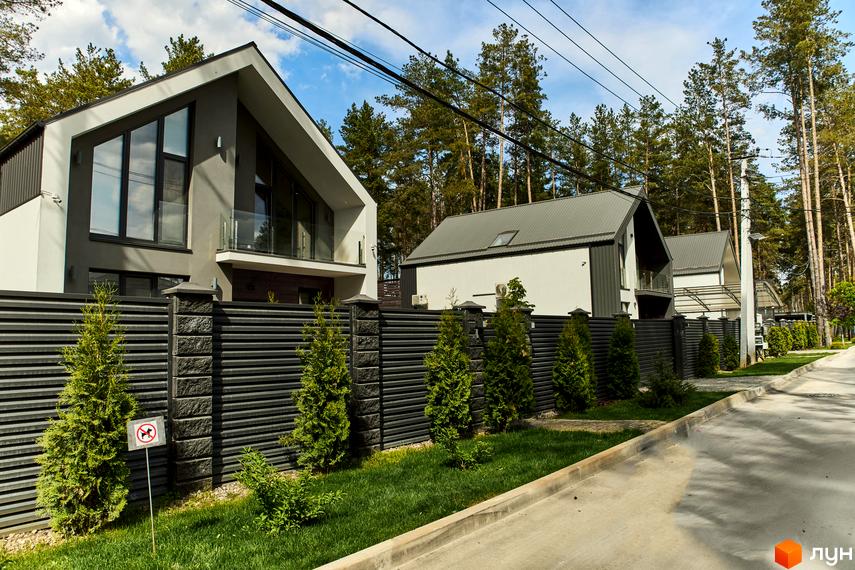 Котеджне містечко Квітка Полонини. Будинки з великими вікнами та балконами, огороджені парканом з зеленими насадженнями. Поруч асфальтована дорога та ліс.