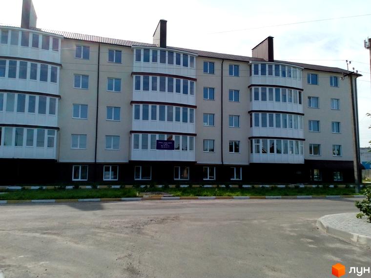 Зовнішній вигляд багатоквартирного будинку ЖК Садовий з балконами та вікнами. Прибудинкова територія з зеленою зоною та дорогою.